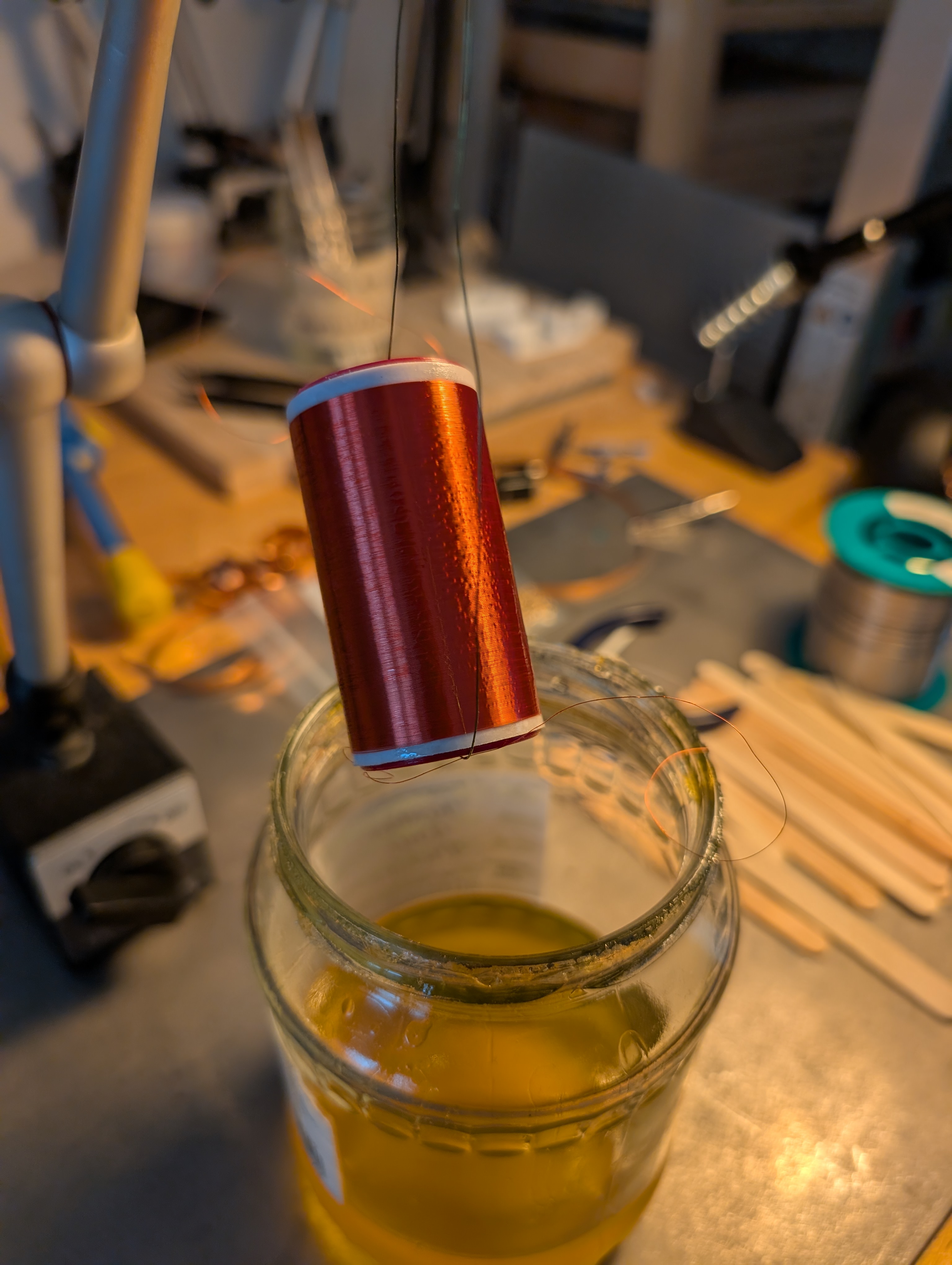 the coil hanging over the shellac pot to drip off any excess